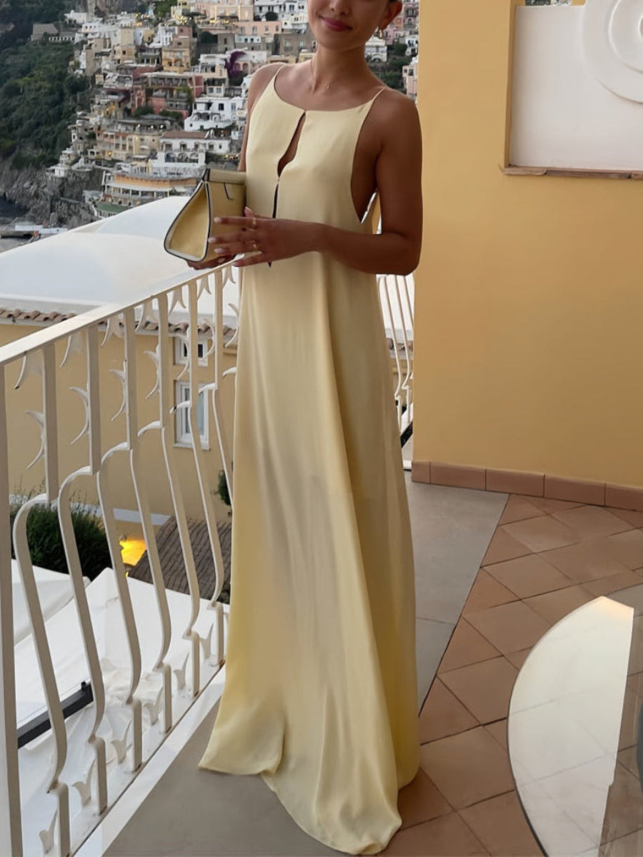 A woman wearing a spaghetti strap, backless, maxi dress in a apricot color, standing on a balcony with a scenic view in the background.